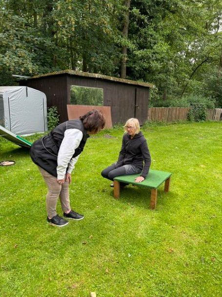 2 Frauen auf dem Hundeplatz, eine sitzt auf einem kleinen Tisch