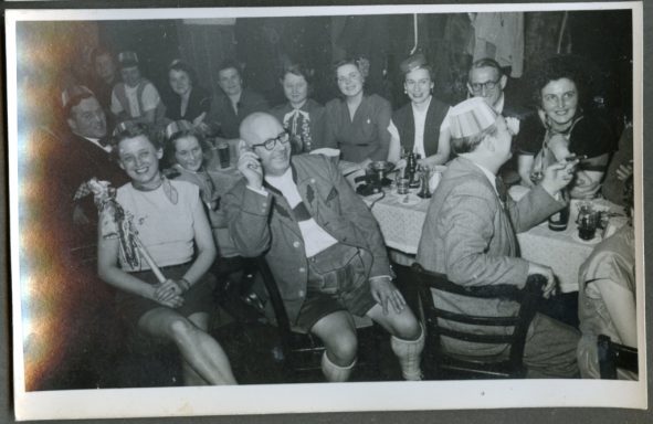 Eine Gruppe von Menschen sitzt an Tischen in einem festlichen Raum, lächelnd und entspannt.