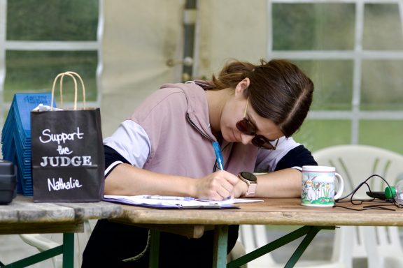 Eine Person in Sonnenbrillen schreibt an einem Tisch, neben einem Beutel und einer Tasse.