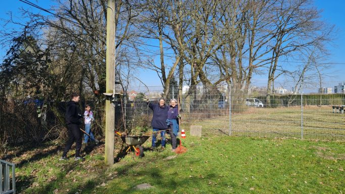 Drei Personen stehen auf einer Wiese, umgeben von Bäumen und einem blauen Himmel.