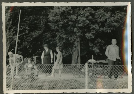Schwarzweißfoto einer Gruppe von Personen vor einem Zaun im Freien.