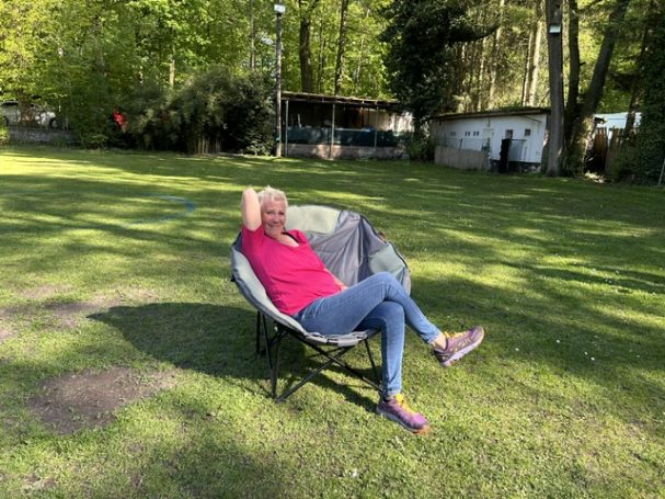 Eine Person mit blonden Haaren sitzt entspannt in einem Stuhl im Grünen.