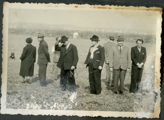 Eine Gruppe von sechs Menschen steht auf einem Feld, alle in formeller Kleidung.