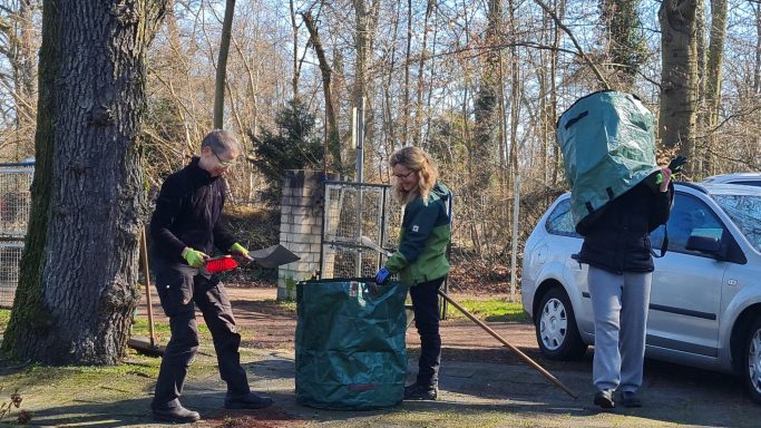 Drei Personen sammeln Müll in der Natur, während sie Müllsäcke und Werkzeuge verwenden.