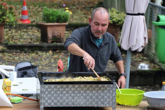 Mann bereitet Essen in einer großen Pfanne im Freien vor.